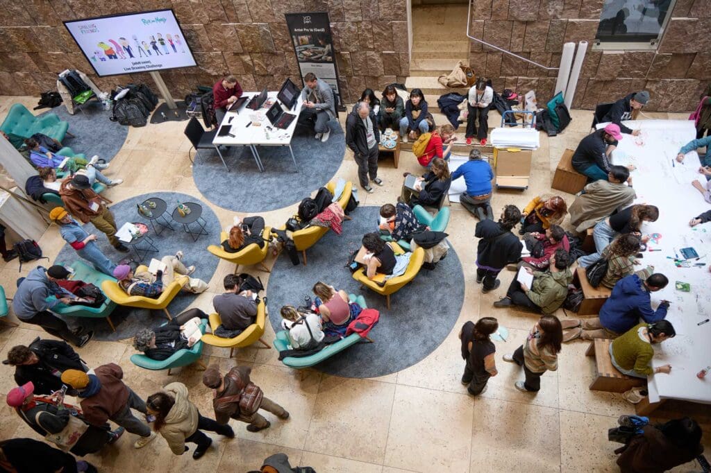 Blick ins Foyer vom Haus der Katholischen Kirche Stuttgart von oben. Viele Menschen sitzen in bunten Sesseln und unterhalten sich.