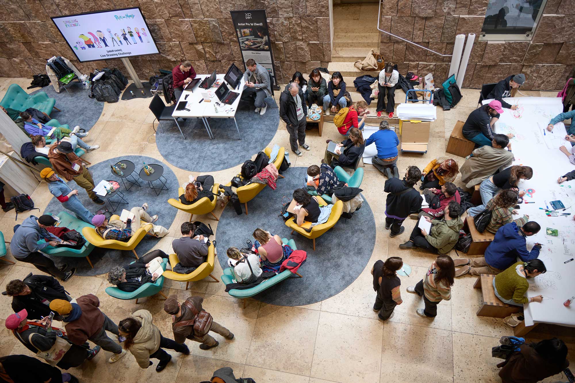 Blick ins Foyer vom Haus der Katholischen Kirche Stuttgart von oben. Viele Menschen sitzen in bunten Sesseln und unterhalten sich.