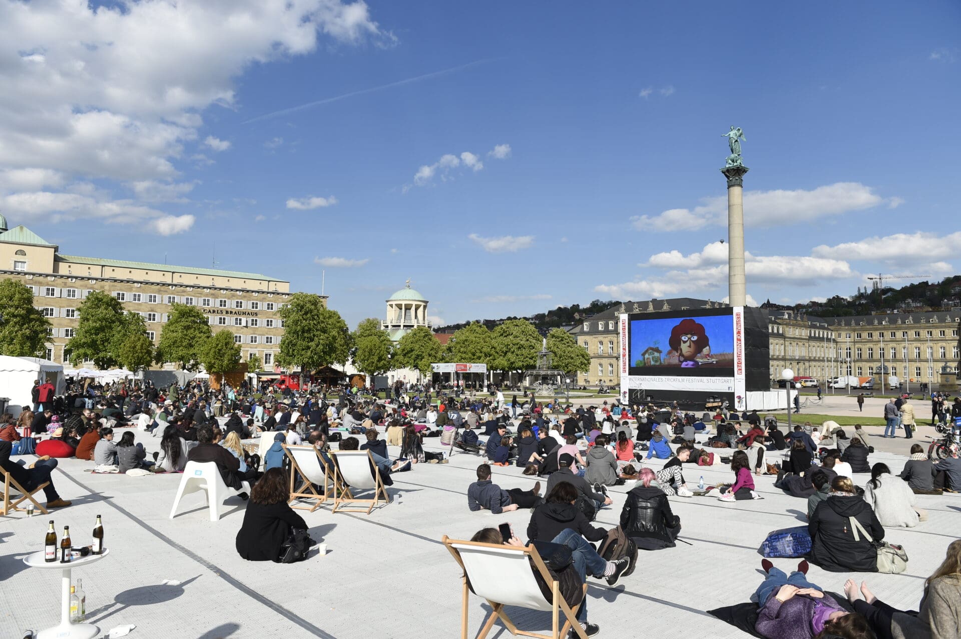 Viele Menschen sitzen auf dem sonnigen Schlossplatz und schauen einen Film
